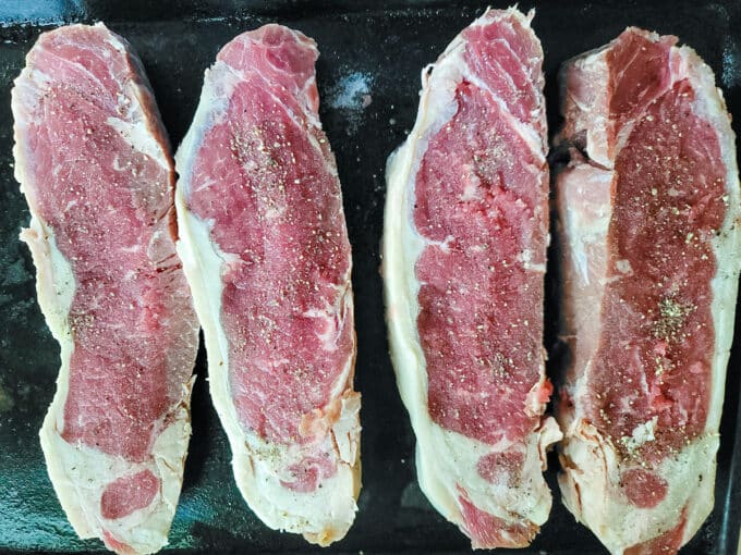 Seasoned steaks on baking sheet.