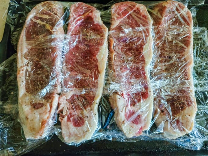 Steaks covered with plastic wrap.