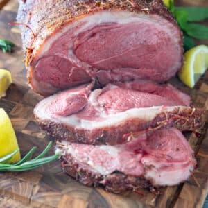 Sliced leg of lamb on wooden board.
