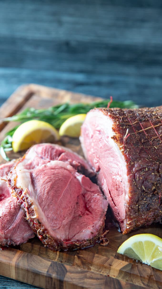 Rare sliced lamb on a wooden board with fresh herbs and lemon.