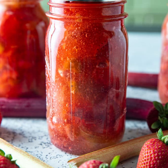 Jars of strawberry rhubarb pie filling with fresh rhubarb and berries.