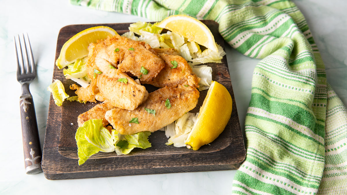 Fish on a bed of lettuce served with lemon slices.