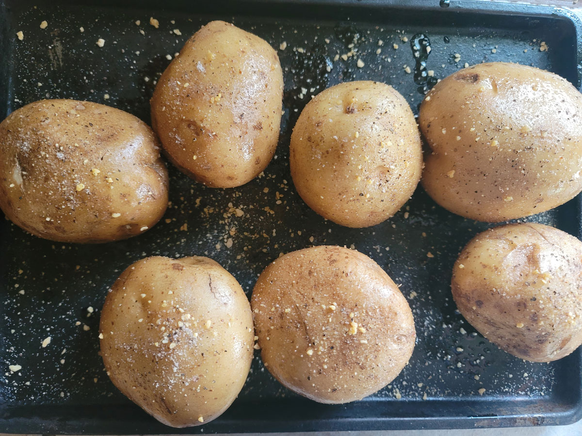 Potatoes rubbed with oil and spices on a baking sheet.