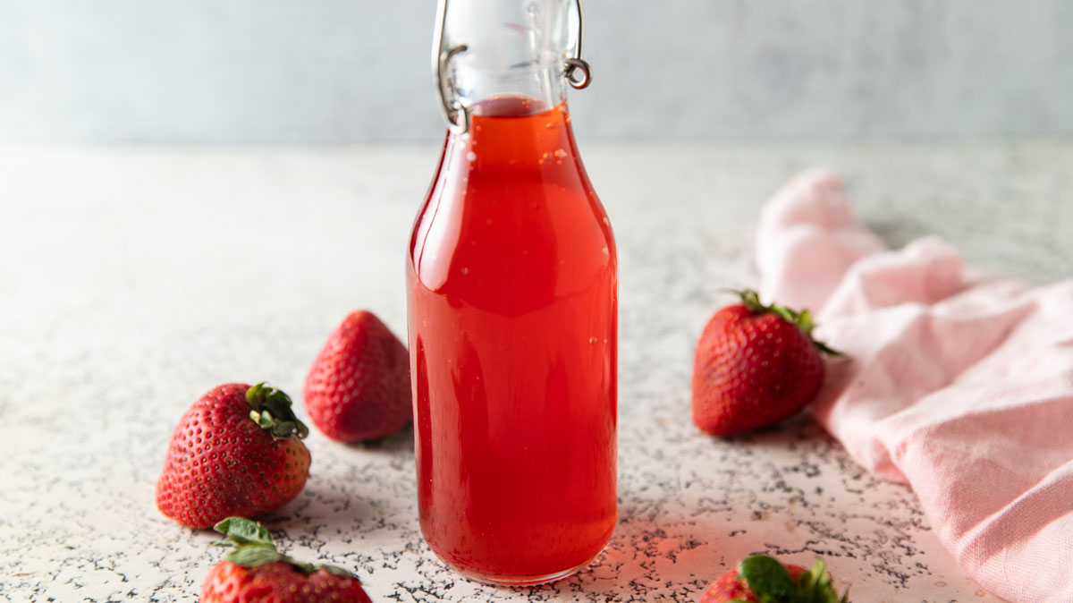 Bottle of vinegar with fresh strawberries on the board.