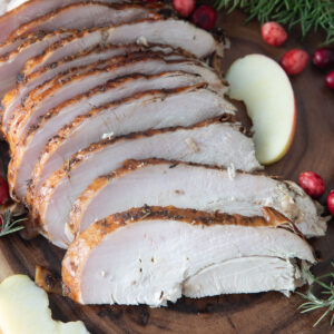 Sliced turkey breast on wood with sliced apples and fresh cranberries.