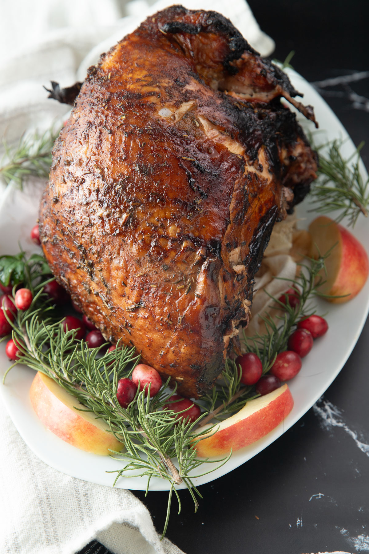 Whole smoked turkey breast on a white platter with garnishes.