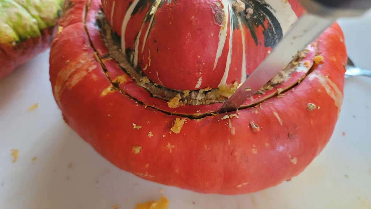 Knife cutting down into squash to remove the cap.