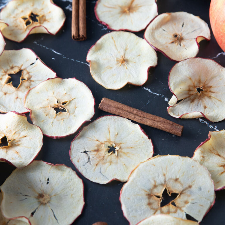 Overhead photo of dried apple chips on a black board.
