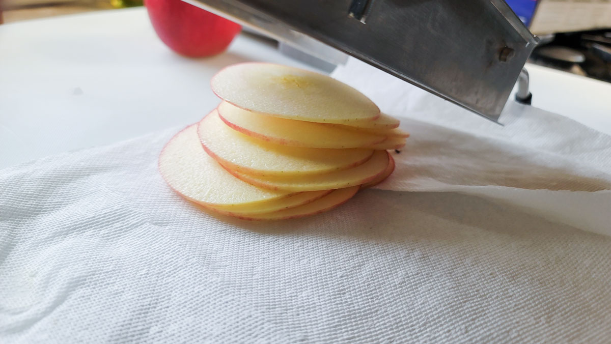 Sliced apples in a pile under a mandolin.
