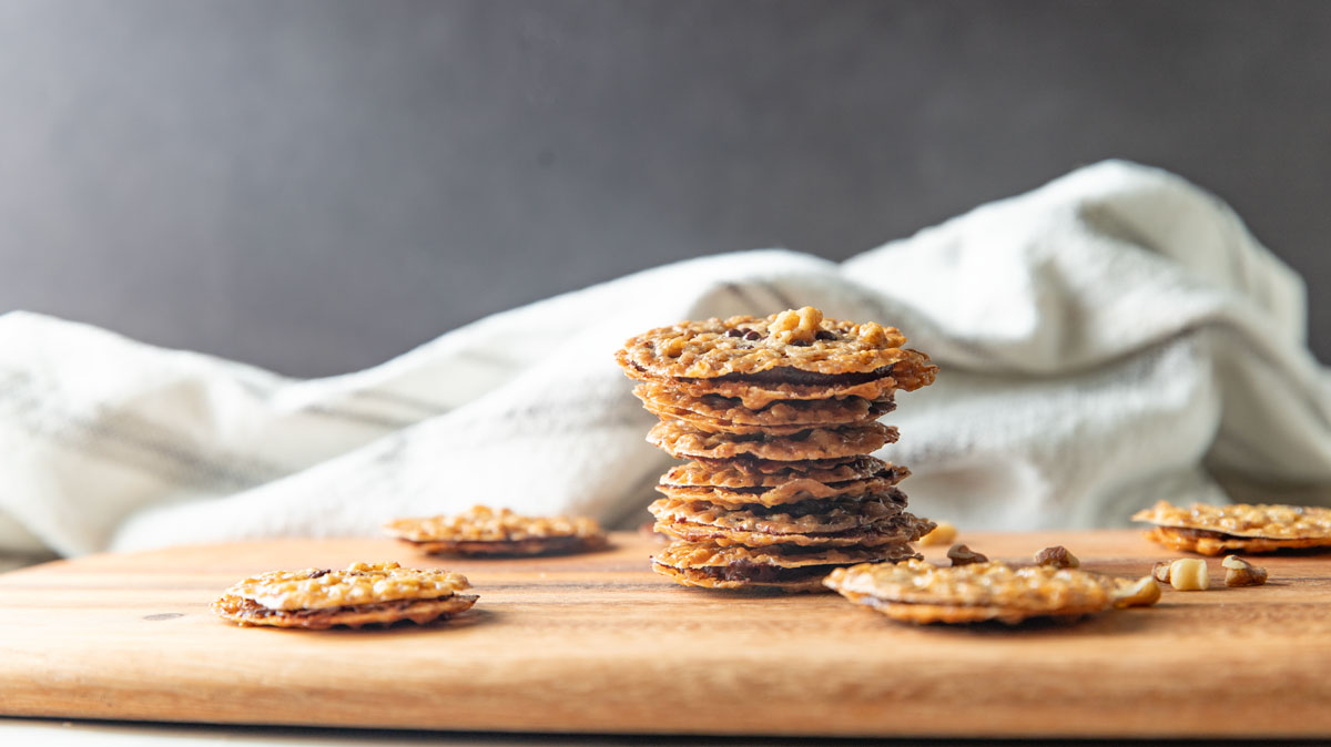 Pile of stacked lace cookies on a wooden cutting board.