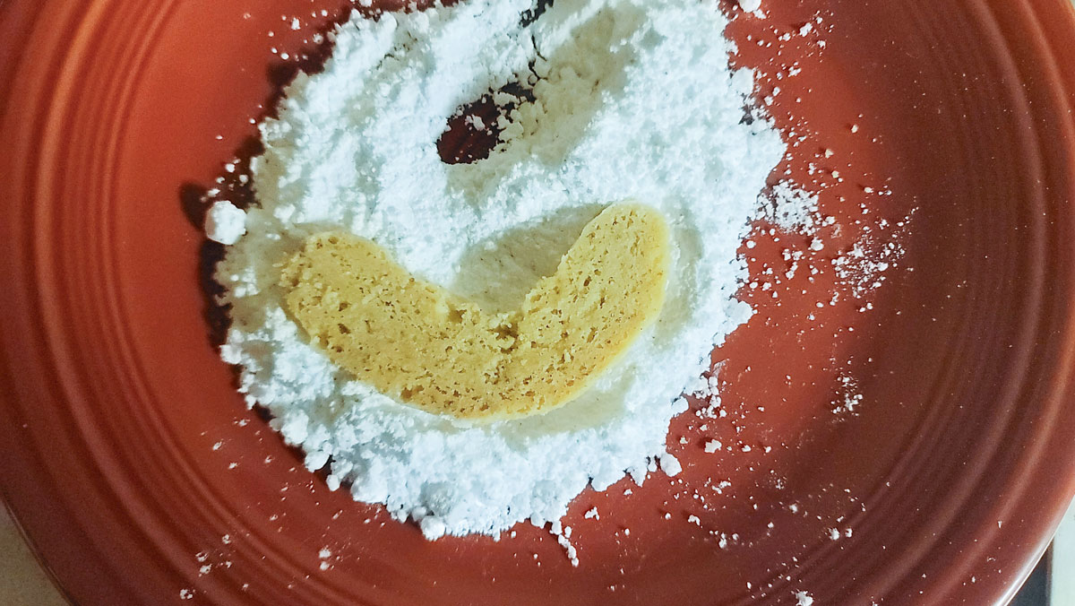 Powdered sugar on a plate with a cookie being rolled in it.