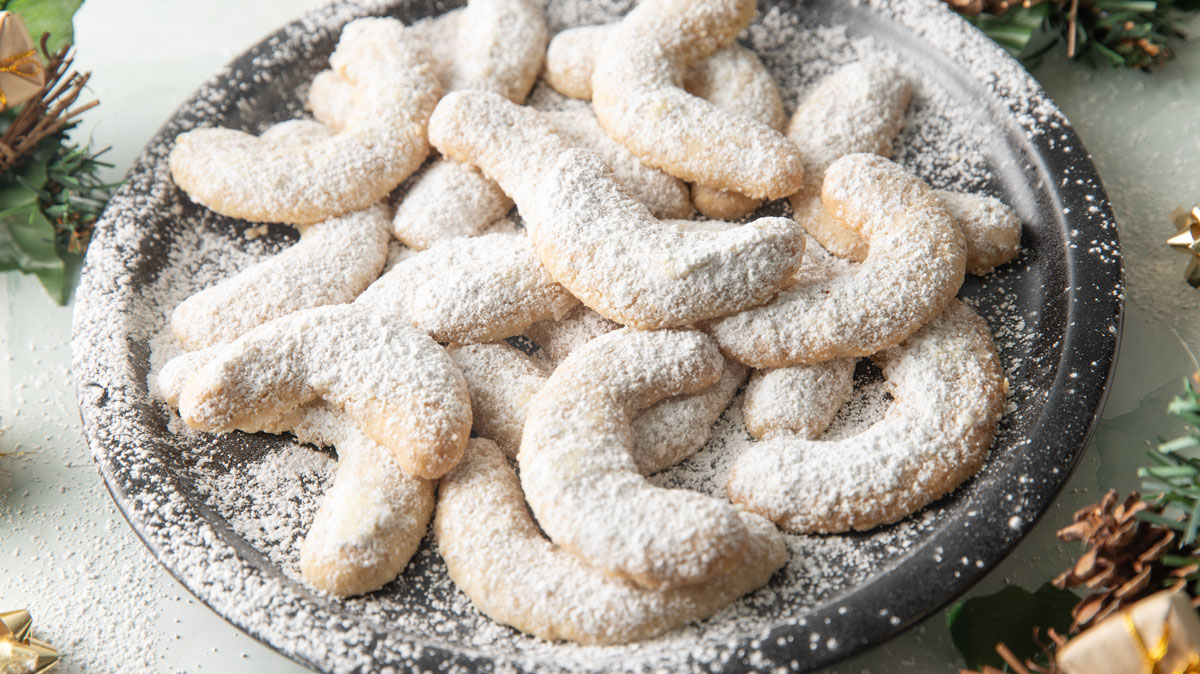 Vanilla crescent cookies dusted with powdered sugar next to Christmas decorations.