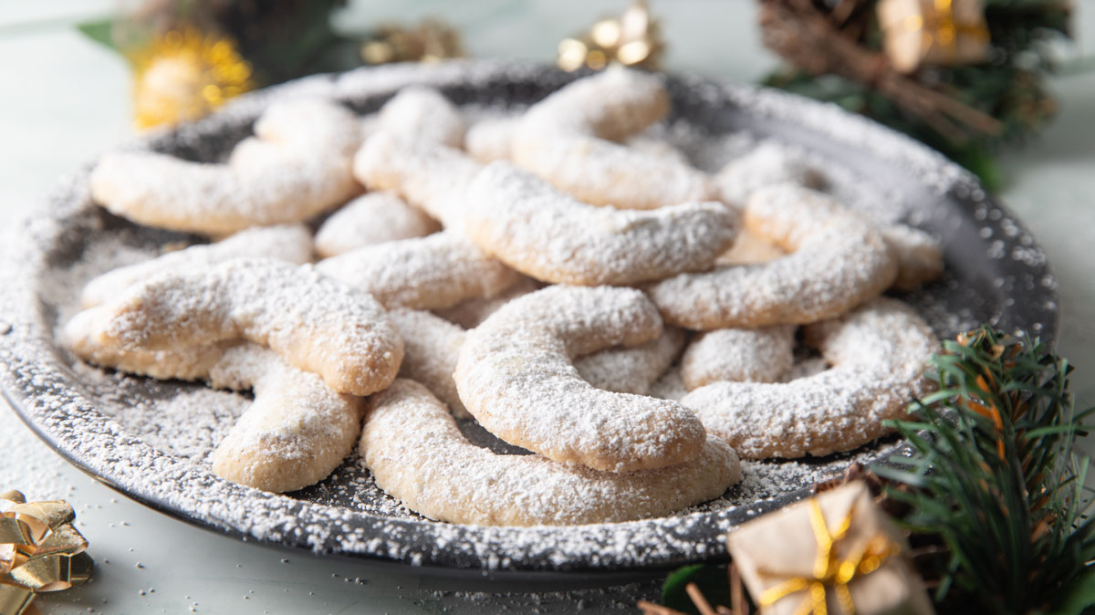 Vanilla crescent cookies on a black plate dusted with confectioner sugar.