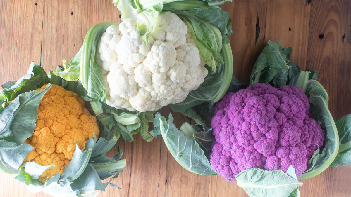 Three colorful heads of cauliflower on a wooden board.