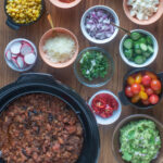 Crockpot with chili and small bowls with various toppings.