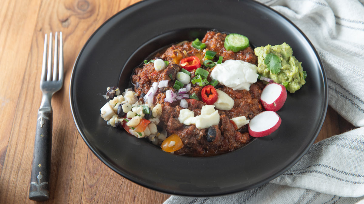 Large bowl of chili with colorful toppings.