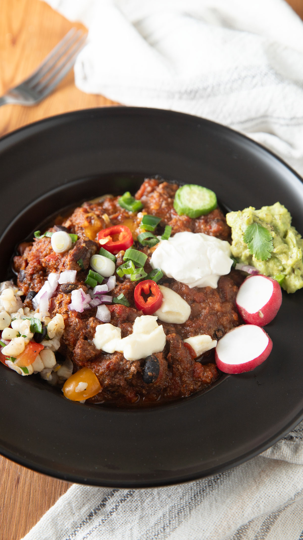 Black bowl filled with chili and various toppings.