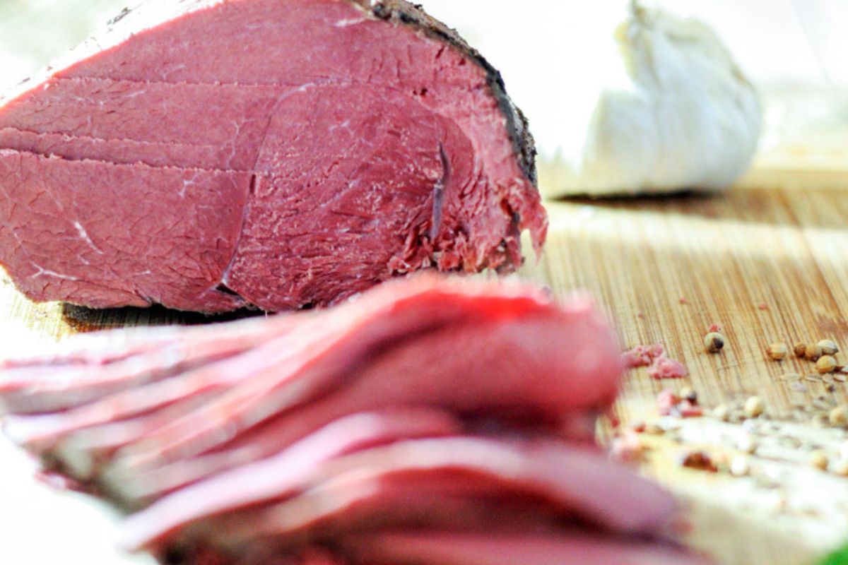 Bit cut of venison back leg, corned, with slices stacked in front of it on a cutting board.