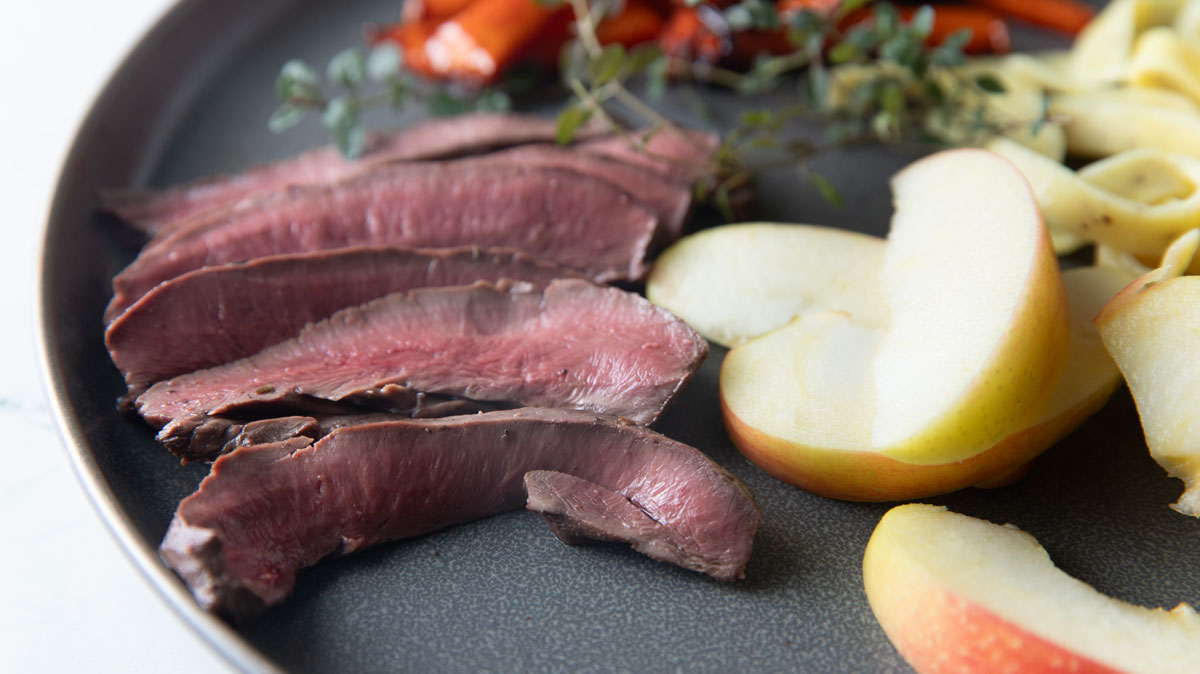 Venison heart sliced on a plate with sliced apples.