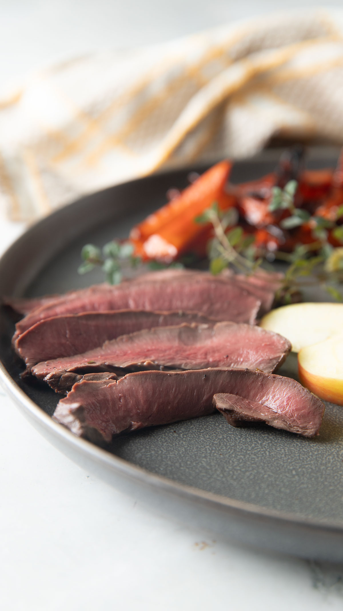 Sliced deer steaks with side dishes on a gray plate.