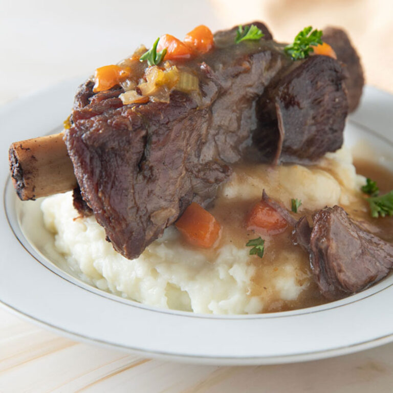 Beef Rib on top of a bowl of mashed potatoes with gravy.