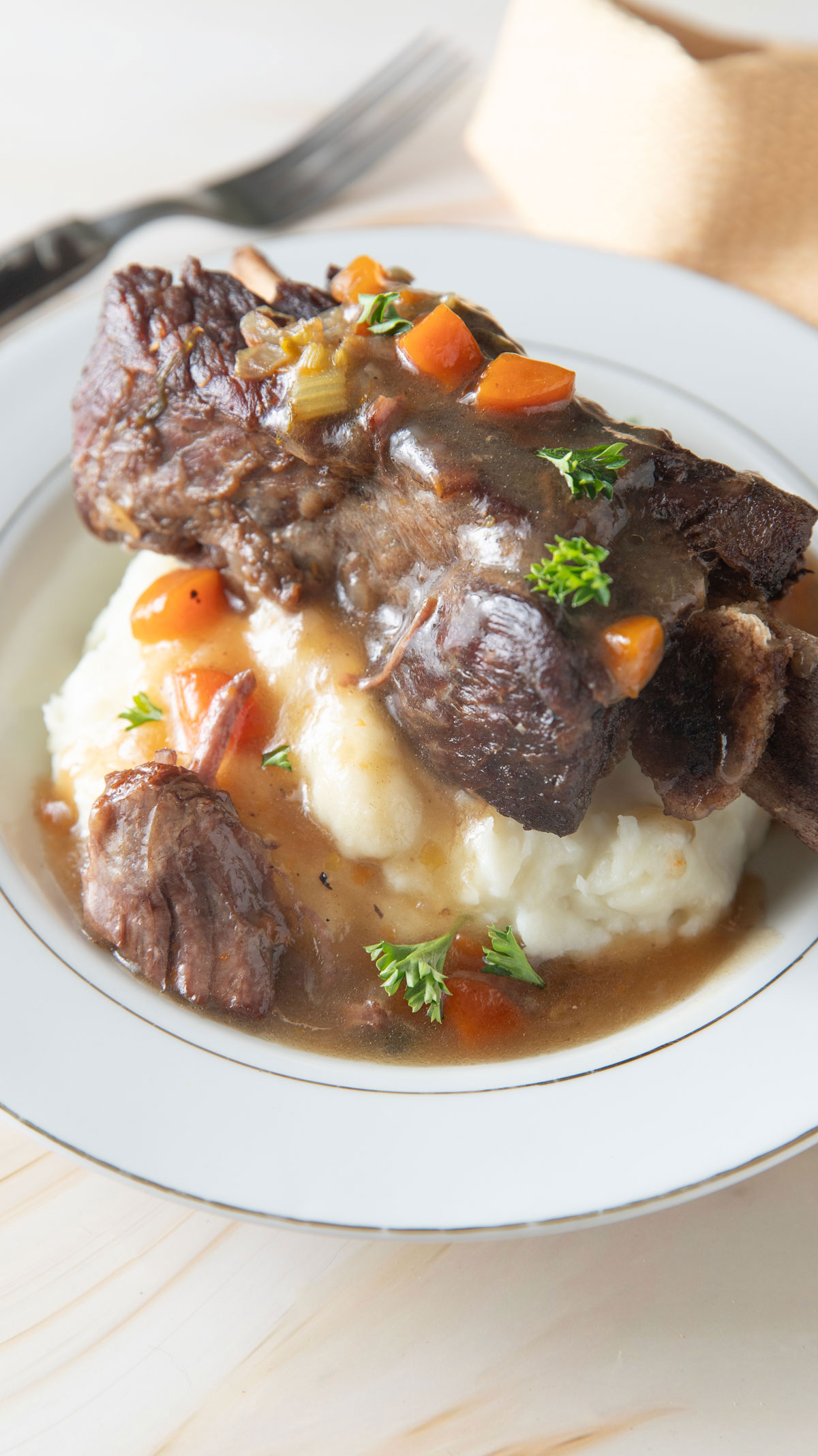 Close up of beef rib with potatoes and veggies.