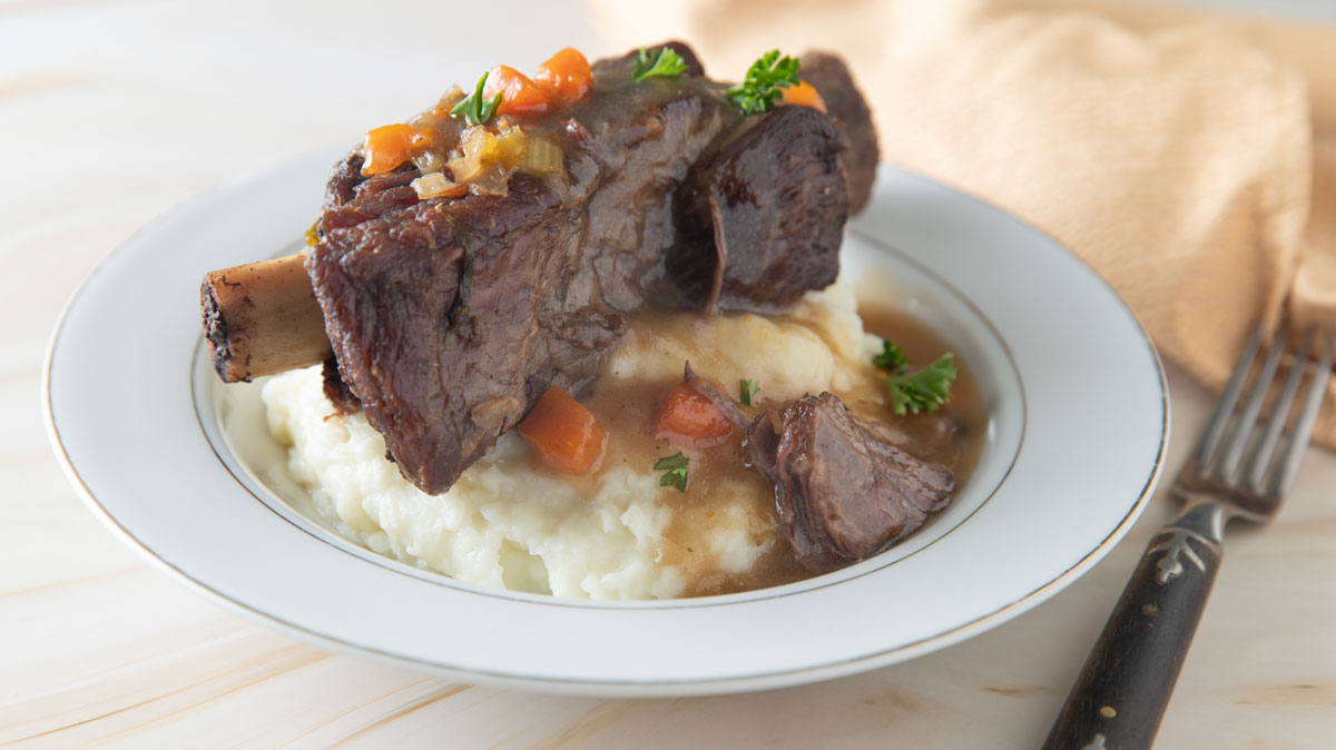 Beef rib sitting on a bed of mashed potatoes with lots of gravy.
