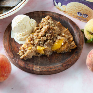 Slice of peach pie on a wooden plate.