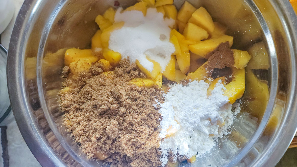 Ingredients for peach pie filling added to a stainless bowl.