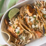 Salmon tacos in an oval bowl with lime wedges.