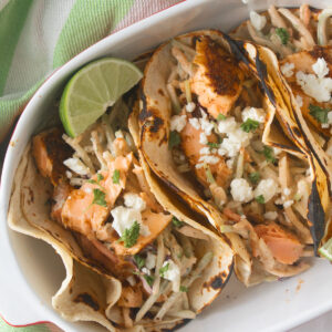 Salmon tacos in an oval bowl with lime wedges.