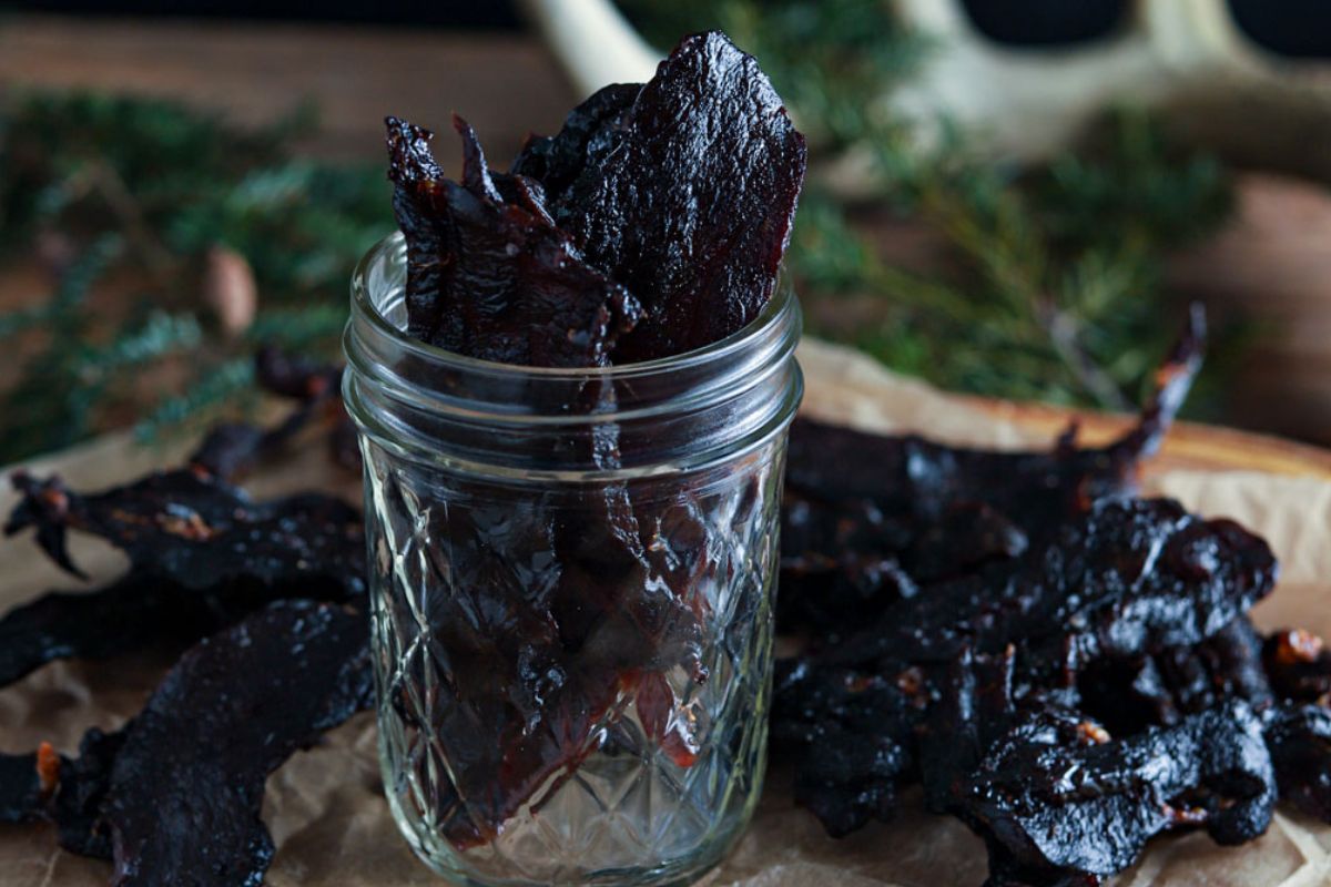 Bites of venison jerky in and around a mason jar.