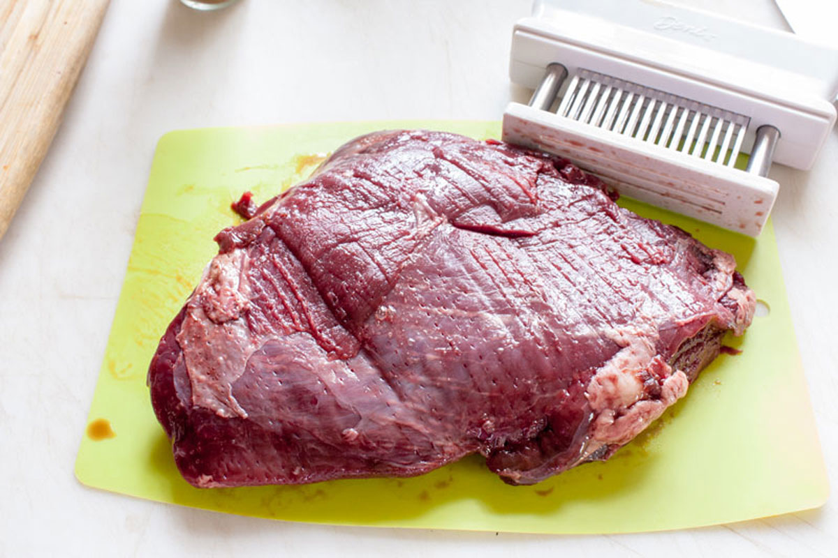 Meat being tenderized with a bladed tenderizer.