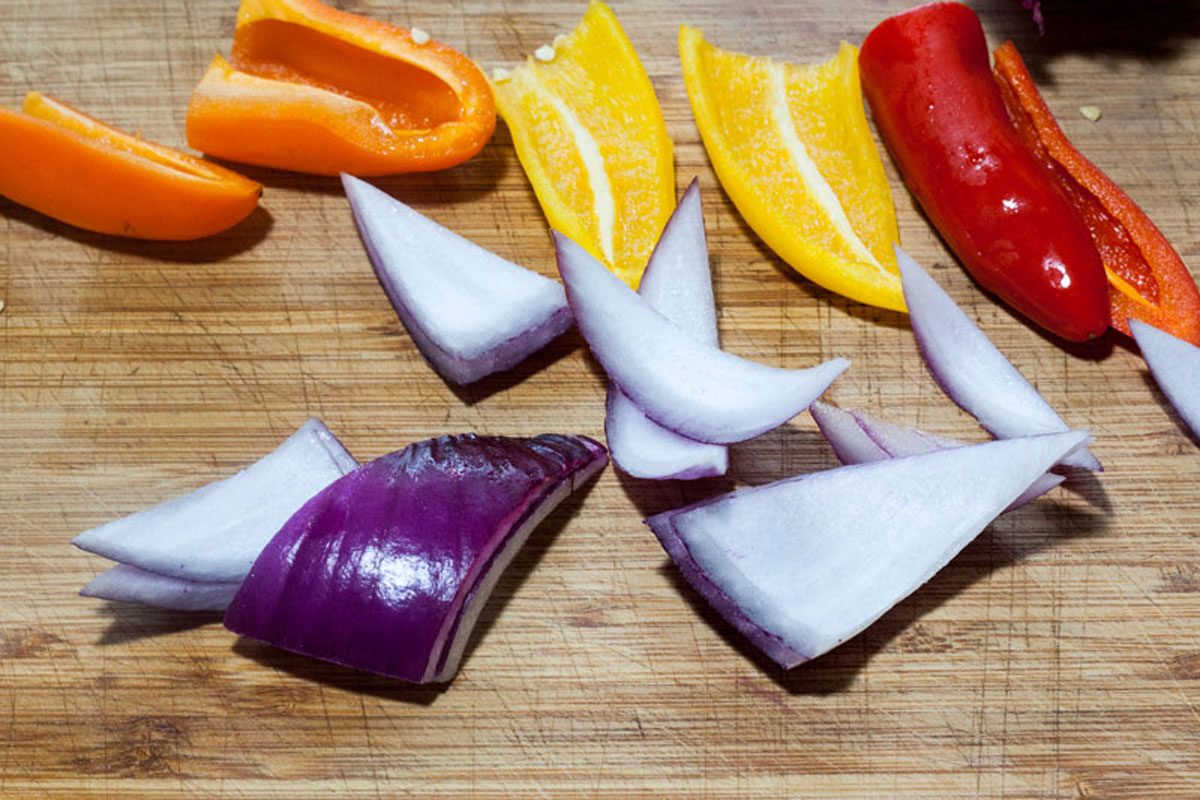 Peppers and onions cut up on a cutting board.