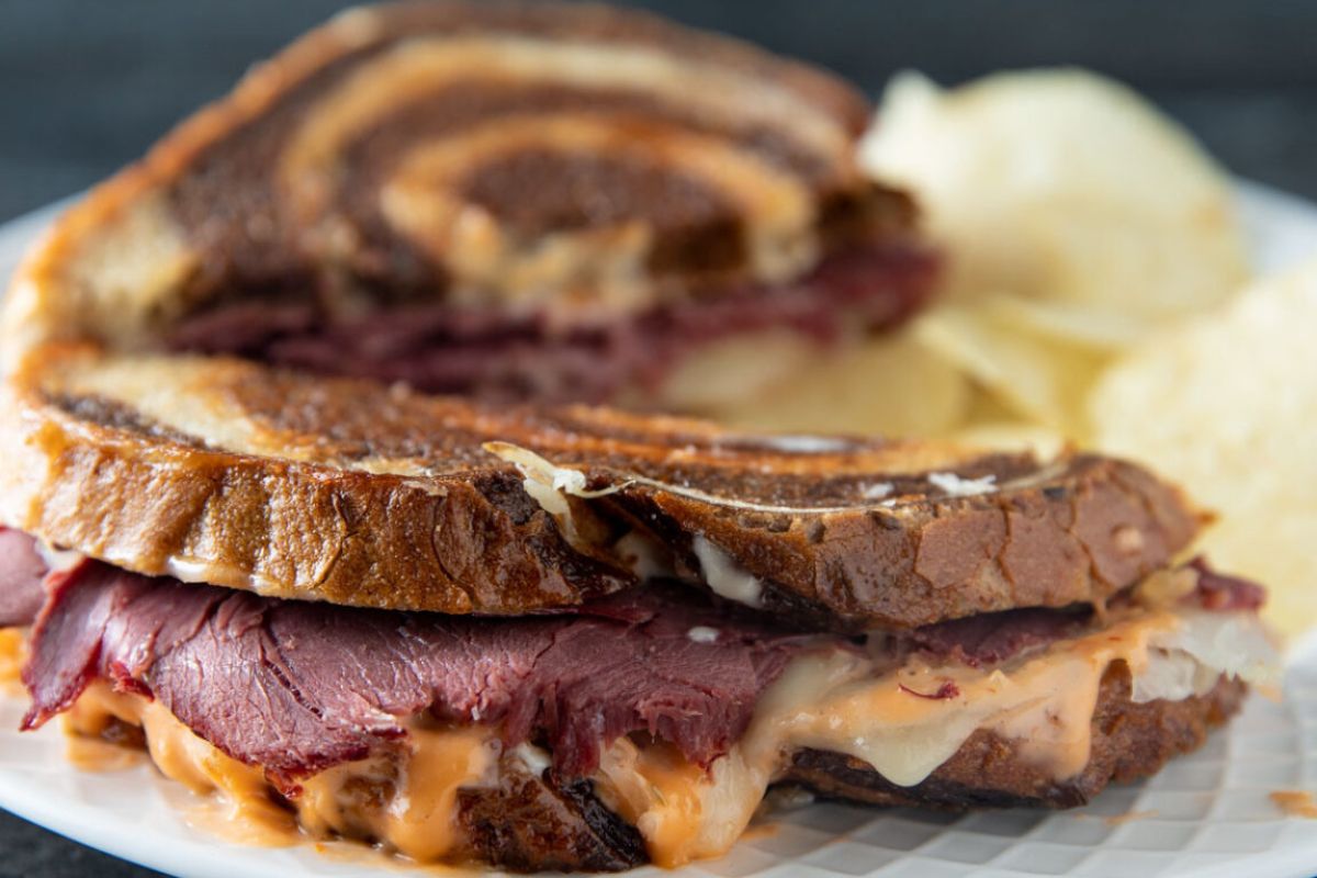  A Reuben sandwich made with marbled rye with melted cheese and thousand island dripping from it.