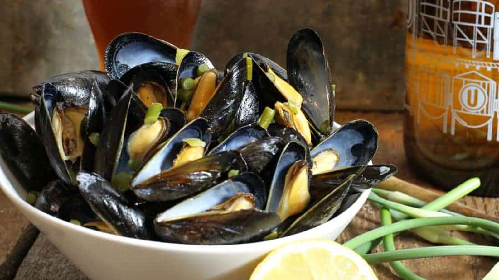 Bowl of steamed mussels next to garlic scapes.