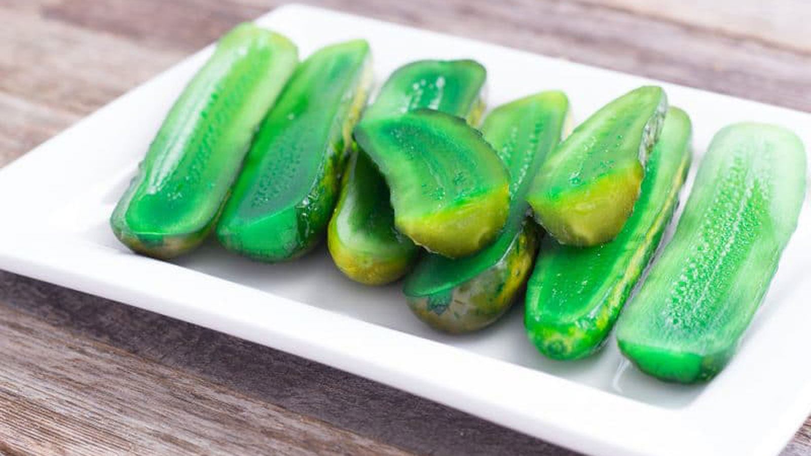 Green Kool-aid pickles on a white plate.