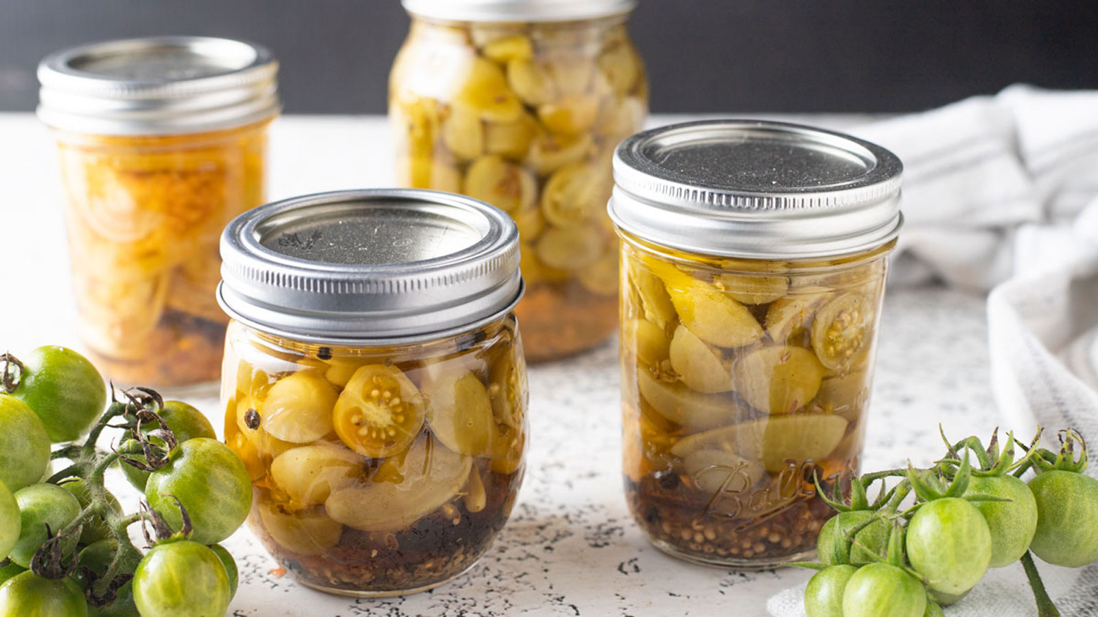 Jars of pickled green tomatoes on white board.