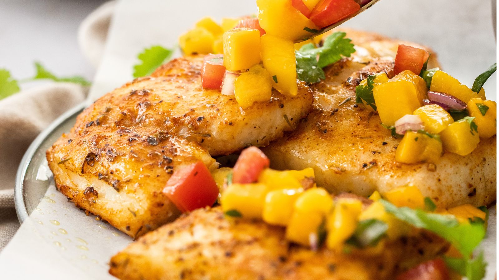 Big chunks of mahi mahi fish served on a plate with a colorful salsa.