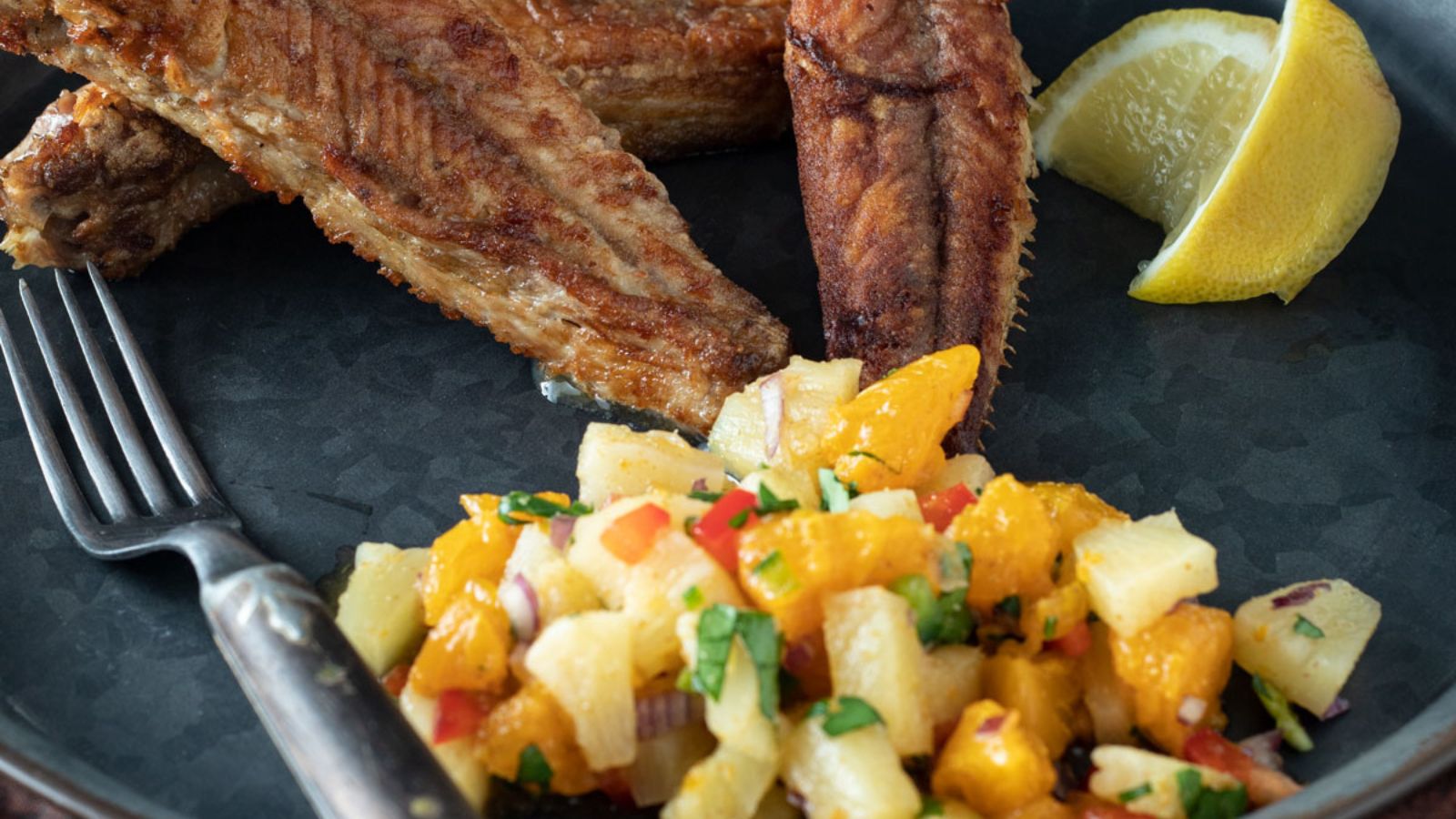 Citrus salsa on a dark plate next to bullhead fish.