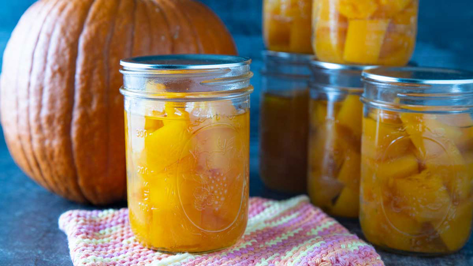 Canned pumpkin in jars with fresh pumpkin in the background.