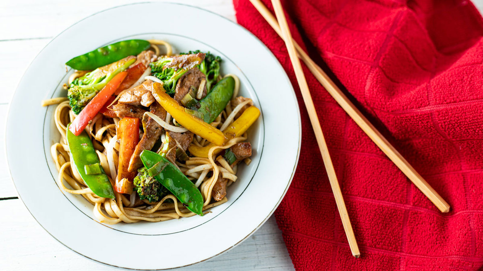Colorful chicken lo mein in a white bowl.