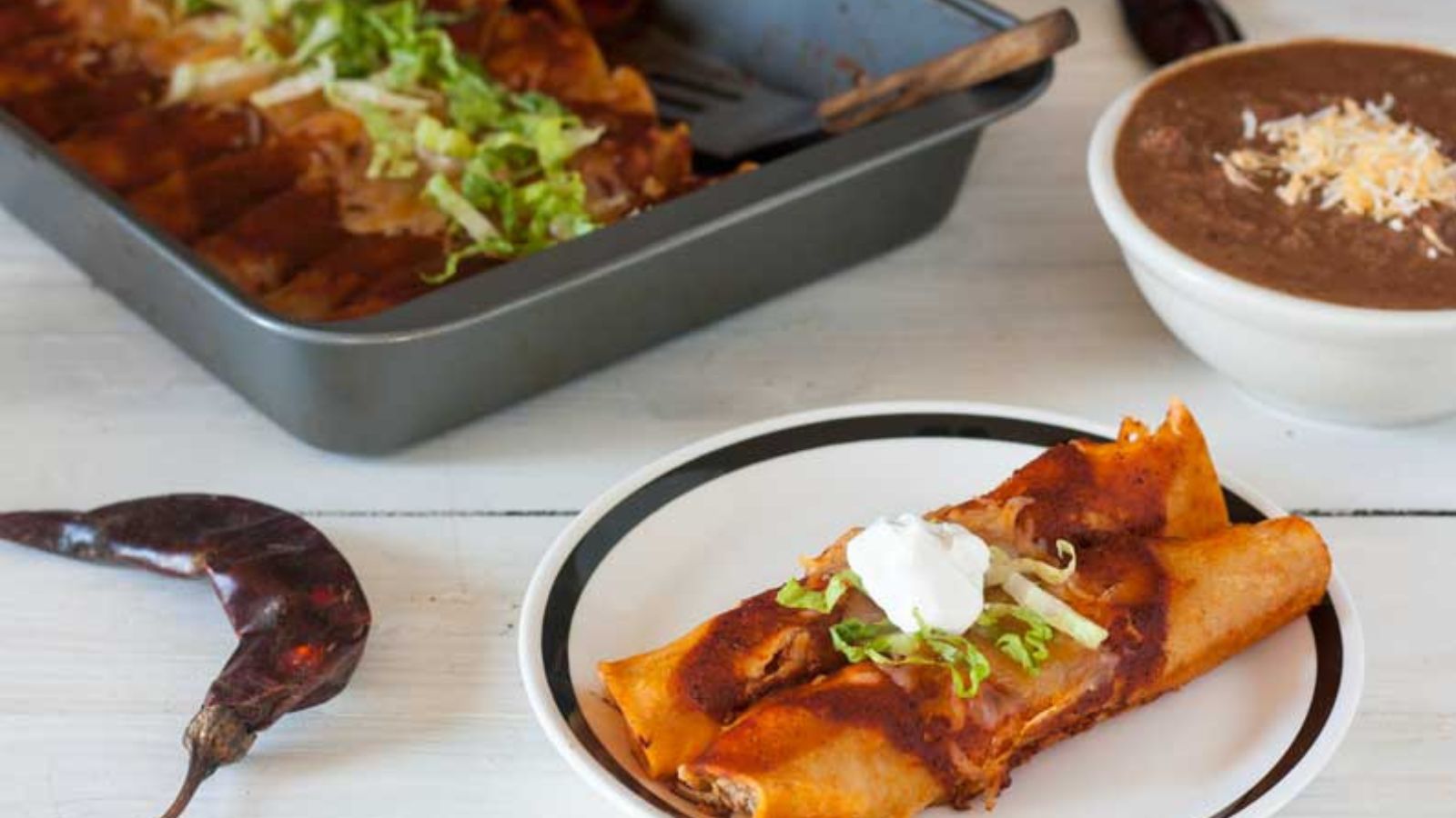 2 chicken enchiladas on white plate with black rim