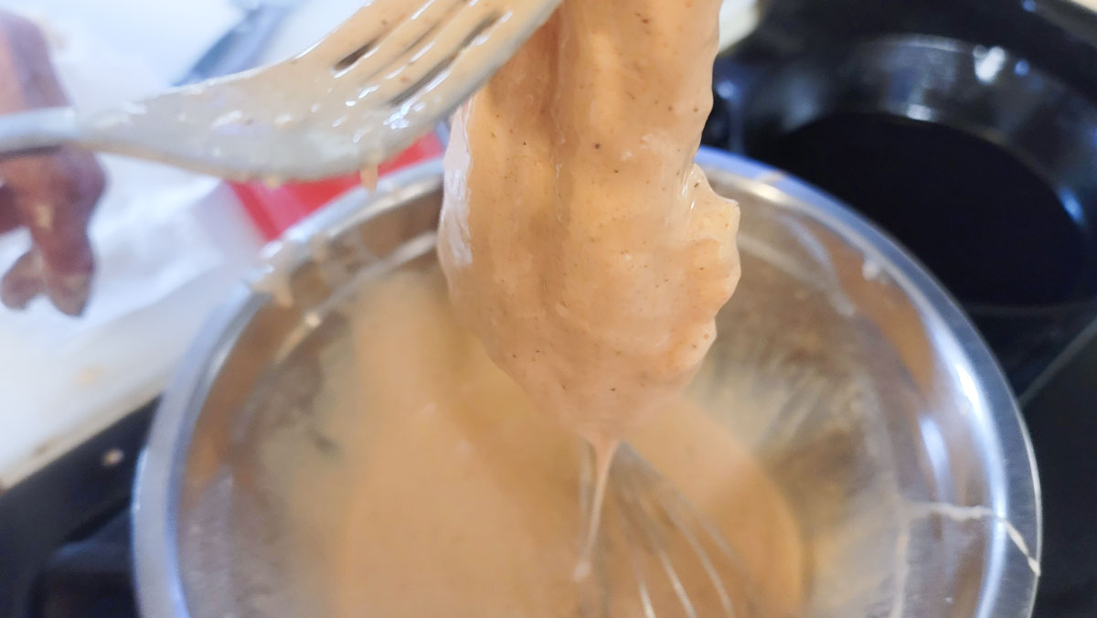 Fish covered in batter, dripping into the bowl.