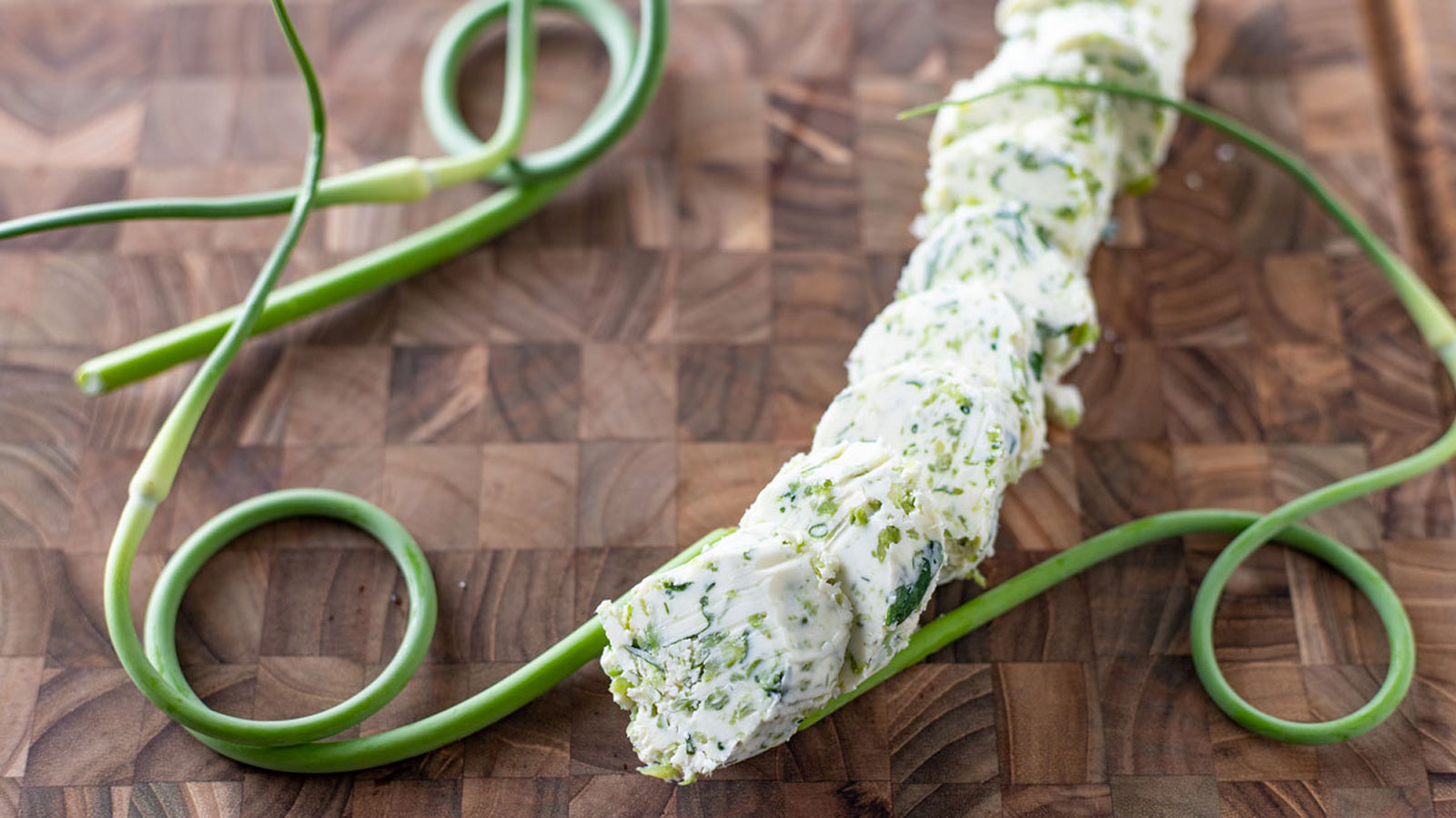 Slice garlic butter on a cutting board with garlic scapes