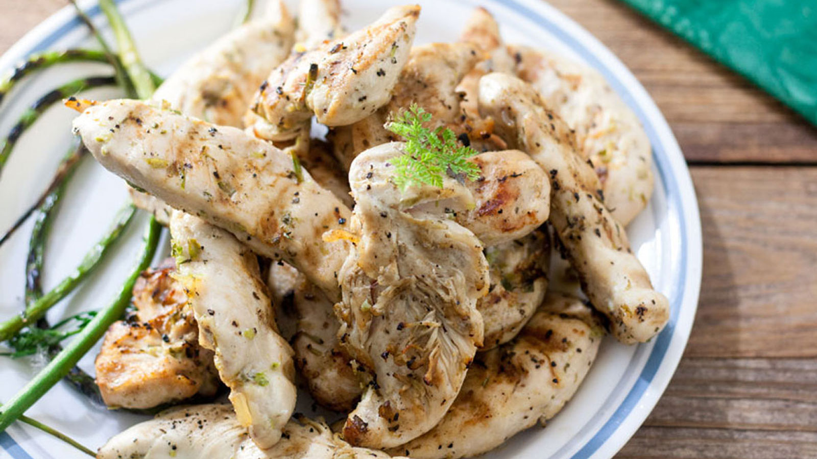 Chicken tenders piled on a plate with grilled garlic scapes.