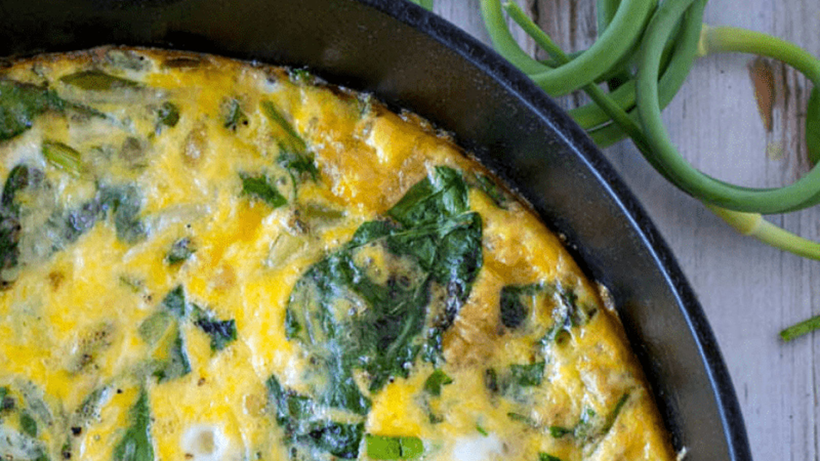 Frittata with spinach and scapes in a cast iron skillet.
