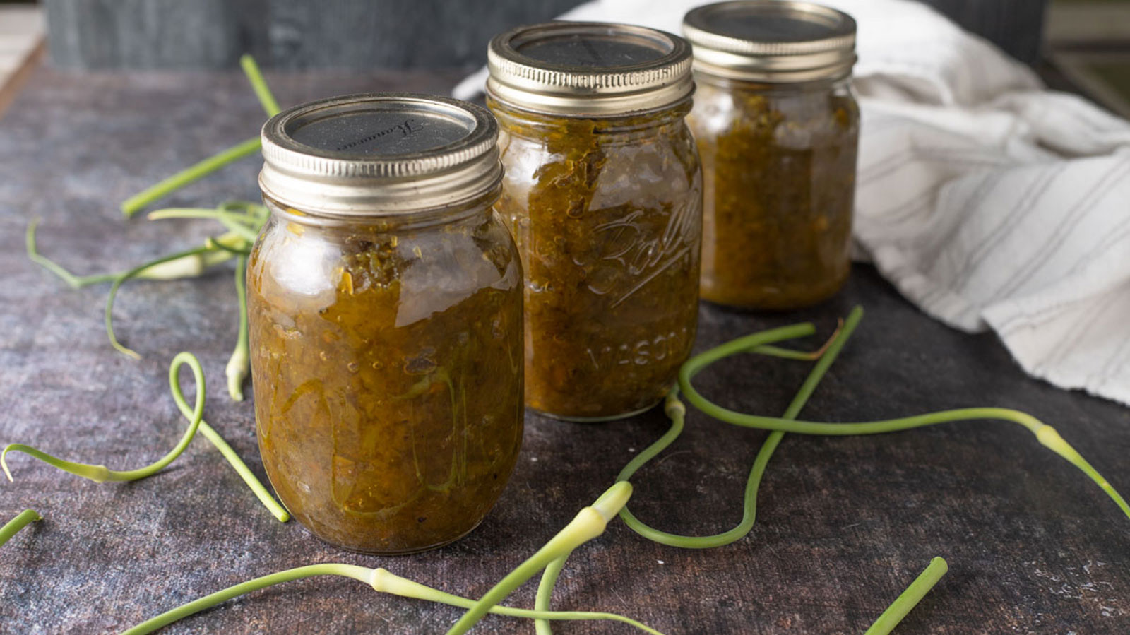 Jars of garlic scape relish with fresh scapes.