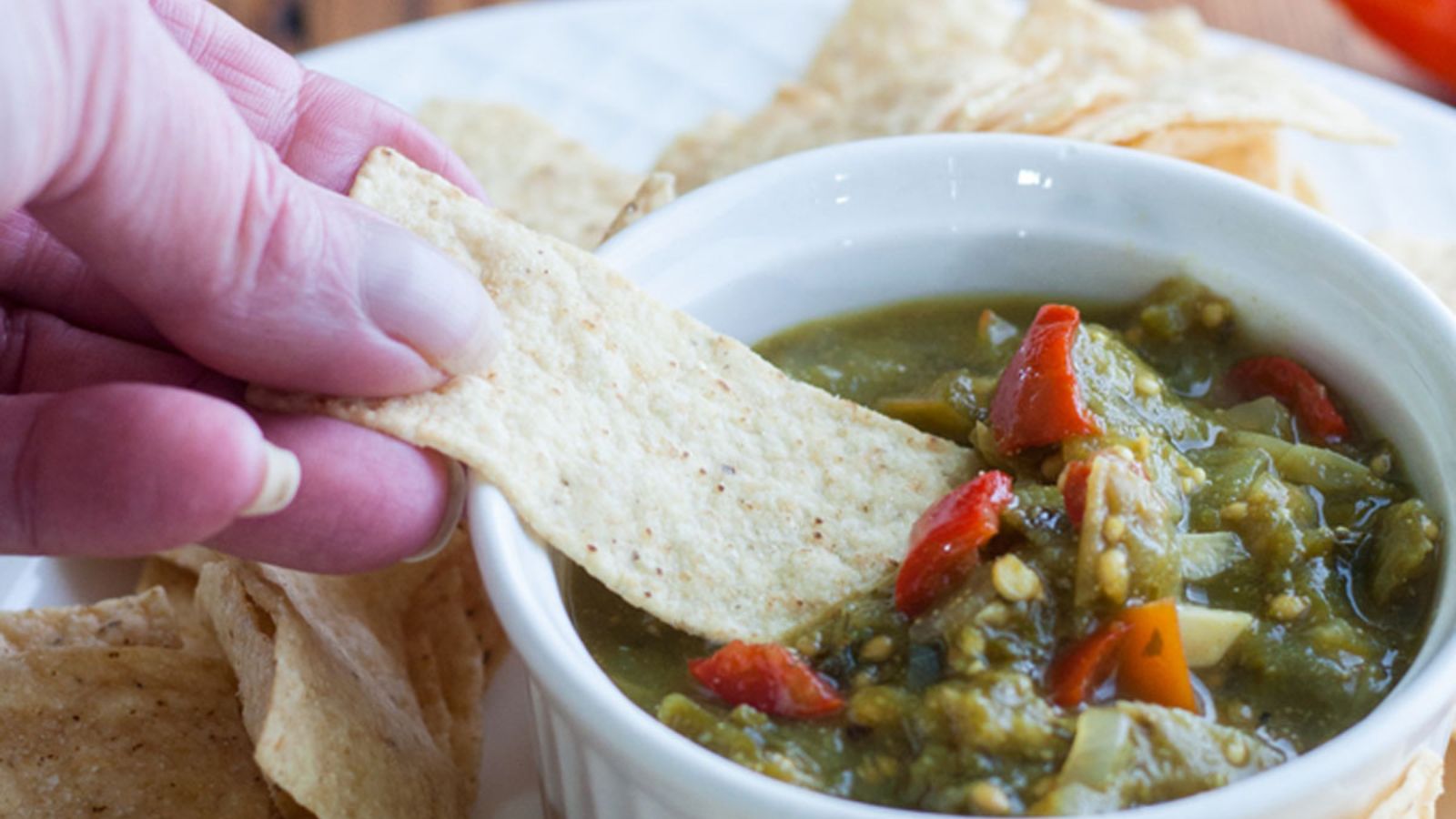 Green tomato salsa being scooped up with a tortilla chip by a woman hand.