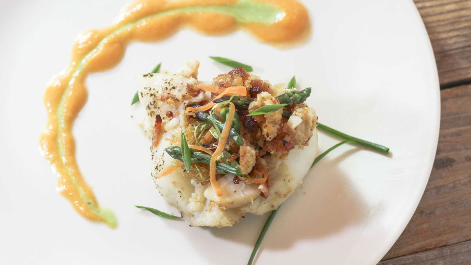 Bacon Horseradish Lobster Stuffed Grouper fish on a white plate garnished with asparagus and carrot shavings.